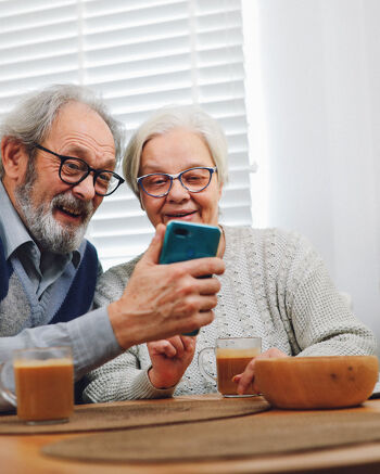 Two elderly people sharing a moment over a smartphone at the kitchen table