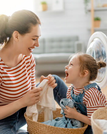 Person and child doing laundry together beside an open washing machine